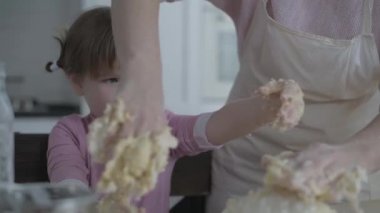 Mom teaches daughter to cook the dough. The girl learns to cook pastries. Kneading the dough together. Roll out the dough for baking. A wonderful family in the spacious kitchen prepares food. Holiday cooking sweets. Little helper in the kitchen.