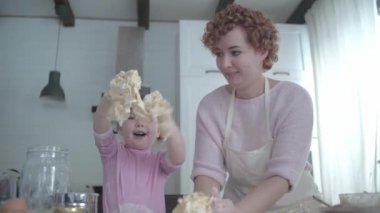 Anne kızına hamur pişirmeyi öğretiyor. Kız yemek yapmayı öğreniyor. Birlikte diz çöküyoruz. Hamuru pişirmek için yuvarla. Geniş mutfakta harika bir aile yemek hazırlar. Tatil tatlısı pişirmek. Kızı annesine yardım ediyor. Mutfakta küçük bir yardımcı..