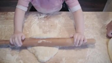 Mom teaches daughter to cook the dough. The girl learns to cook pastries. Kneading the dough together. Roll out the dough for baking. A wonderful family in the spacious kitchen prepares food. Holiday cooking sweets. Little helper in the kitchen.