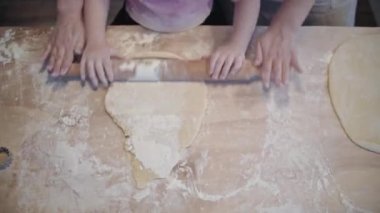Mom teaches daughter to cook the dough. The girl learns to cook pastries. Kneading the dough together. Roll out the dough for baking. A wonderful family in the spacious kitchen prepares food. Holiday cooking sweets. Little helper in the kitchen.