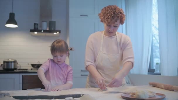小女儿帮妈妈在厨房里烘焙 用饼干切割机切饼干 把面团放在烤盘上 把饼干的空白处铺在烤纸上 — 图库视频影像