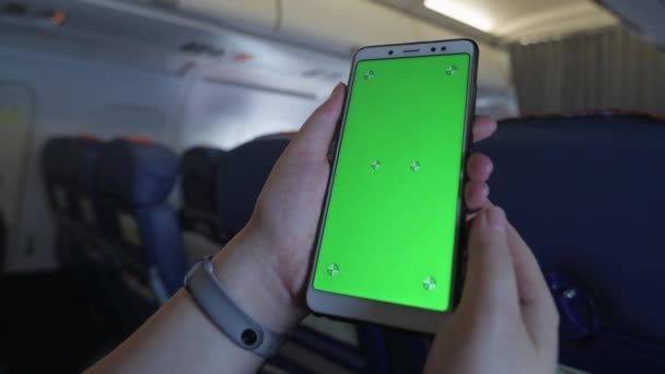 女孩坐在小木屋里 绿色屏幕智能手机特写 装置在飞机上 飞行期间在飞机上休息 飞机上的手机在绿色屏幕上打转和拍手 — 图库视频影像