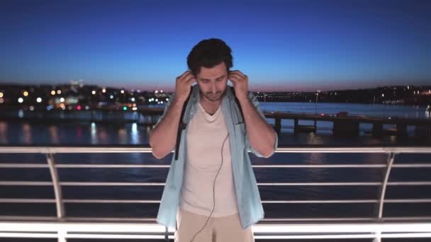 一个年轻人戴上耳机 打开手机上的音乐 在这个城市的背景下 一个人在跳舞 听音乐 在伊斯坦布尔的河流和夜晚的背景下跳舞 — 图库视频影像