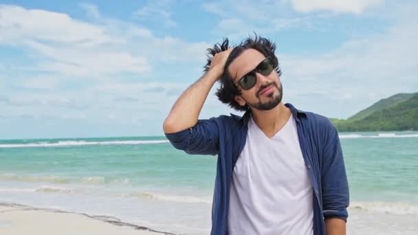 海の背景に若いハンサムな男の肖像画 魅力的な男は笑っている きれいなビーチで贅沢な休息 風の中で毛が発達 — ストック動画