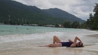 Kumsalda mayo giymiş genç ve güzel bir kız kumsalda yatıyor. Ayaklar havada. Tropik bir adada kumsal. Beyaz kumlu sahilde oynaşan bir kız.