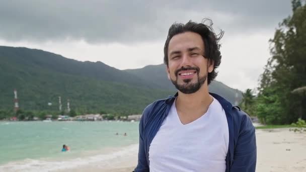 熱帯の島のビーチで若いハンサムな男 白いTシャツを着たセクシーな男がカメラを見ている かわいいブラジル人やアラブ人の笑顔 — ストック動画