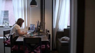Genç güzel kadın bir dizüstü bilgisayarda çalışıyor. Gülümseyen kız öğretmen online dersler veriyor. İş videosu konferansı. Ofis evde. Kişisel izolasyon koşullarında çalış.