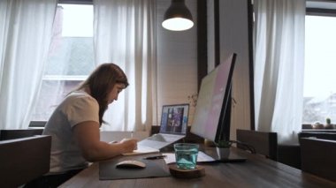 Genç ve güzel bir kadın dizüstü bilgisayarda çalışıyor. Gülümseyen kız öğretmen online dersler veriyor. İş videosu konferansı. Ofis evde. Kişisel izolasyon koşullarında çalış.