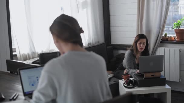 两个漂亮的多族裔女孩在家里工作 自由职业者一起工作 年轻漂亮的女人正坐在笔记本电脑前 它看着手提电脑的屏幕 在网上冲浪 现场通信 — 图库视频影像