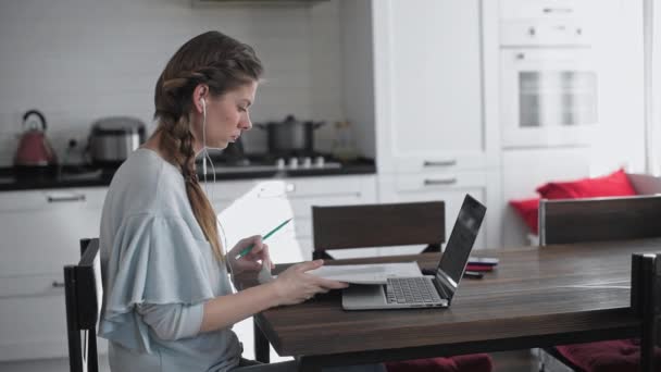 女孩坐在家里的桌子前的笔记本电脑 在家工作 年轻漂亮的女商人在远处工作 检疫期间的远距离学习 — 图库视频影像