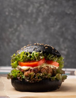 Siyah ekmekli sığır burger, marul, domates ve peynir ile birlikte koyu bir arka planda, kahverengi bir masanın üzerinde servis edilir. Seçici bir odak noktası.