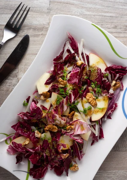 Taze yeşil salata karışımı salata turşusu, rezene, kırmızı soğan, beyaz tabakta elmalar çatal ve bıçakla ahşap arka planda. Sağlıklı yeme kavramı.