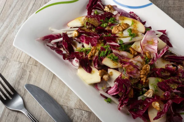 Taze yeşil salata karışımı salata turşusu, rezene, kırmızı soğan, beyaz tabakta elmalar çatal ve bıçakla ahşap arka planda. Sağlıklı yeme kavramı.