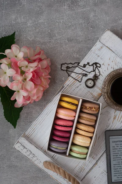 Beyaz ahşap masa zemininde renkli makaronlar bir kutuya konur. Makarnalar yaklaşsın. Bir fincan çay. Pembe çiçekler. Düz üst görünüm. 