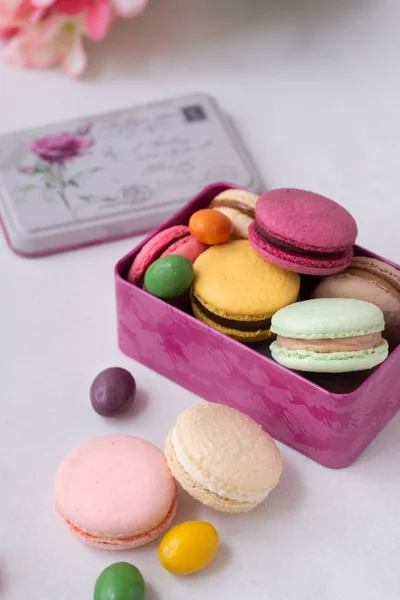 Renkli badem kurabiyeleri ve şekerler beyaz arka planda çiçekli pembe hediye kutusuna konacak. Makaronlar yaklaşsın..