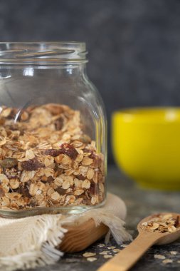 Koyu masada cam kavanozda ev yapımı granola, sarı kase, tahta kaşık. Sağlıklı kahvaltı - granola, süt ve bal. 