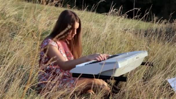 Щаслива молода жінка грає на піаніно на полі — стокове відео