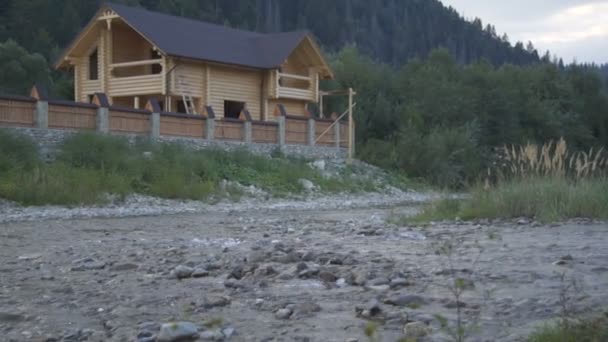 Ein Gebirgsfluss fließt entlang des Waldes und ein schönes Holzhaus — Stockvideo