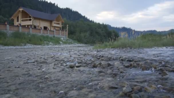 Un río de montaña fluye a lo largo del bosque y una hermosa casa de madera — Vídeos de Stock
