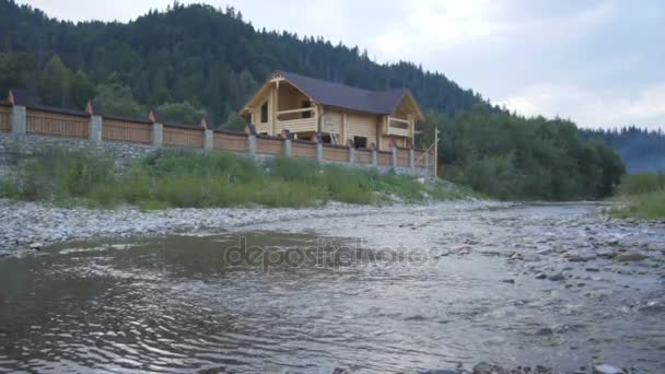 Horská řeka teče podél lesa a krásný dřevěný dům — Stock video