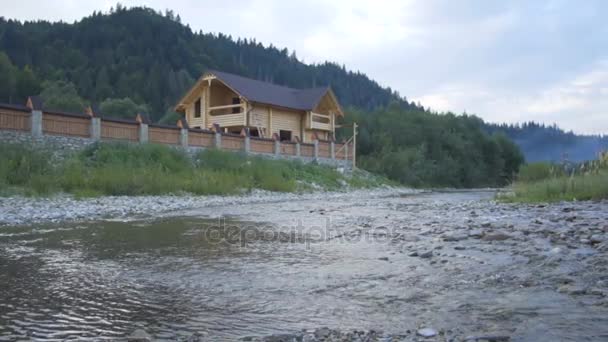 Горная река течет вдоль леса и прекрасный деревянный дом — стоковое видео