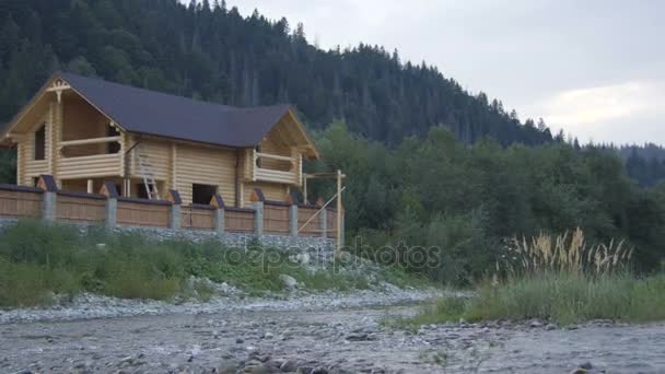 Un río de montaña fluye a lo largo del bosque y una hermosa casa de madera — Vídeo de stock