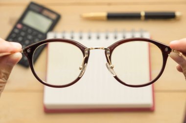 Üstten Görünüm. el gözlük siyah hesap makinesi, tükenmez kalem var, boş defter kağıt bu ahşap koyarak tüm arka plan vardır. Bu görüntü için iş, eğitim ve ekipman kavramı