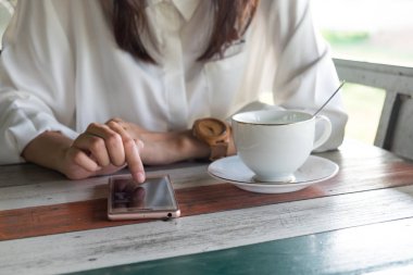 Önden Görünüm. cep telefonu almak sırasında bir ara sabah oynayan genç kadın. ön kahve fincanı ahşap masanın üzerine koyarak sahip. Bu görüntü için iş, teknoloji, içecek ve portre kavramı