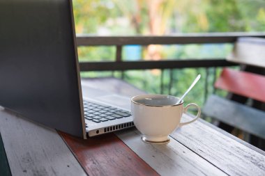 Beyaz kahve Kupası Gümüş kaşık dizüstü bilgisayar tüm her iki koyarak ahşap masanın üzerine koyarak içinde var. doğa arka plan vardır. Bu görüntü için iş ve teknoloji kavramı