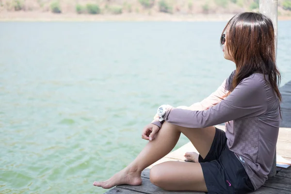 Mujer joven sentada sola en balsa de madera frente a sí misma son fondo de agua azul. esta imagen para viajes, naturaleza y retrato —  Fotos de Stock