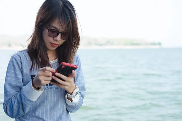 Mujer joven y solitaria jugando al teléfono móvil mientras está de pie y tiene el mar son de fondo. esta imagen para la naturaleza, el retrato y los viajes — Foto de Stock