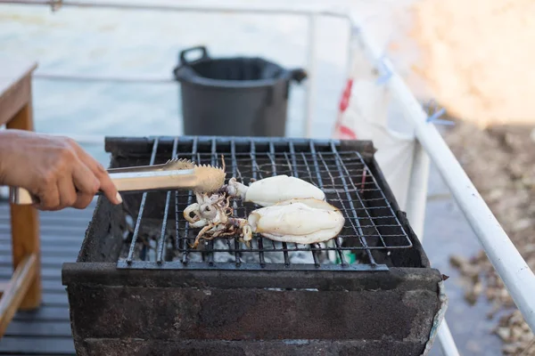 Mão de alguém estão grelhando duas lulas no fogão quente com tong de gelo. esta imagem para o conceito de alimento e animais aquáticos — Fotografia de Stock