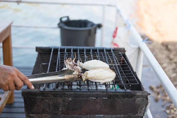hand of someone are grill two fresh squid on stove with ice tong. this image for food and aquatic animals concept