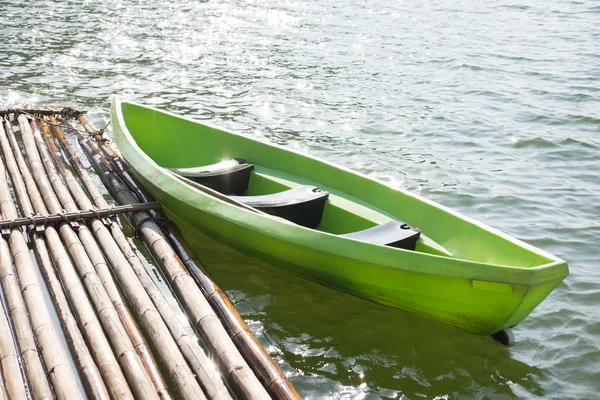 green plastic boat parked at bamboo raft on water surface. this image for travel,nature and vehicle concept