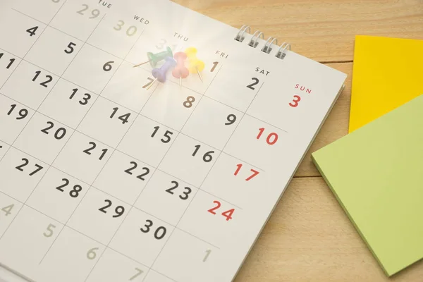 Vista dall'alto. pin mettendo sul calendario desktop e hanno post-it nota messo su accanto a loro. legno sono sfondo. questa immagine per il concetto di accessorio aziendale — Foto Stock