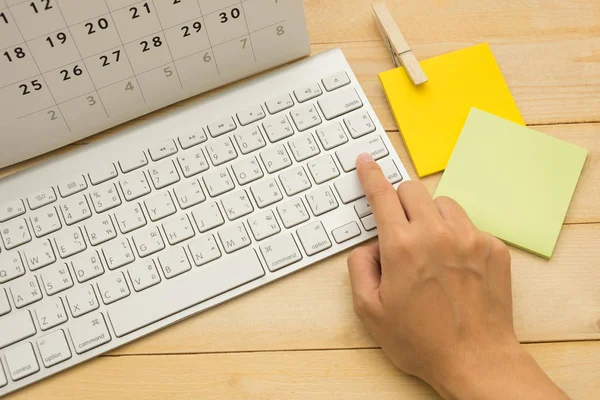 top view. hand of woman typing enter key have calendar putting on top and post-it note putting on beside it. wooden are background. this image for business and education concept