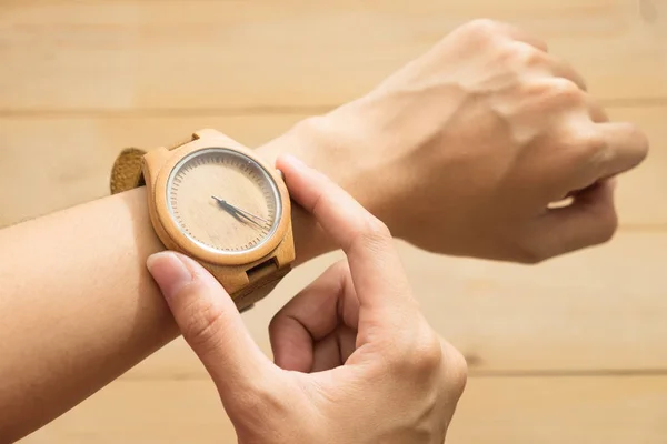 Ansicht von oben. junge Frau stattet hölzerne Armbanduhr am Arm aus und überprüft die Uhrzeit. Holz sind Hintergrund. dieses Image für Ausstattung, Accessoire und Modekonzept — Stockfoto