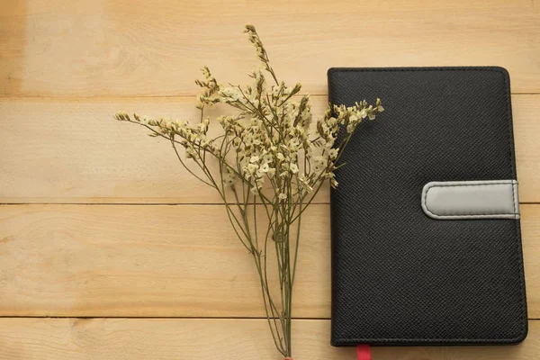 Vista superior. ramo de flores poniendo al lado del libro de cubierta negro y tienen de madera son de fondo. esta imagen para los negocios, la educación y el concepto de flores — Foto de Stock