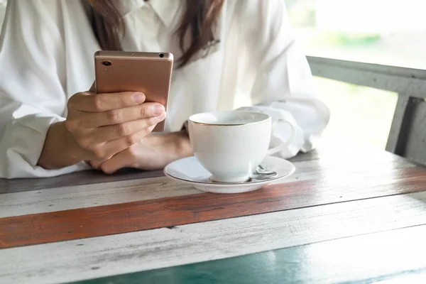Önden Görünüm. cep telefonu almak sırasında bir ara sabah oynayan genç kadın. ön kahve fincanı ahşap masanın üzerine koyarak sahip. Bu görüntü için iş, teknoloji, içecek ve portre kavramı