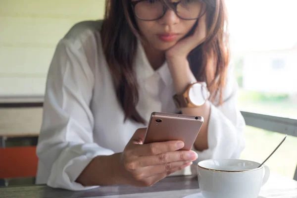 Önden Görünüm. cep telefonu genç bir kadın. o yapmak almak süre ciddi bir yüz bir ara sabah. ön kahve fincanı ahşap masanın üzerine koyarak sahip. Bu görüntü için iş, teknoloji, içecek ve portre kavramı