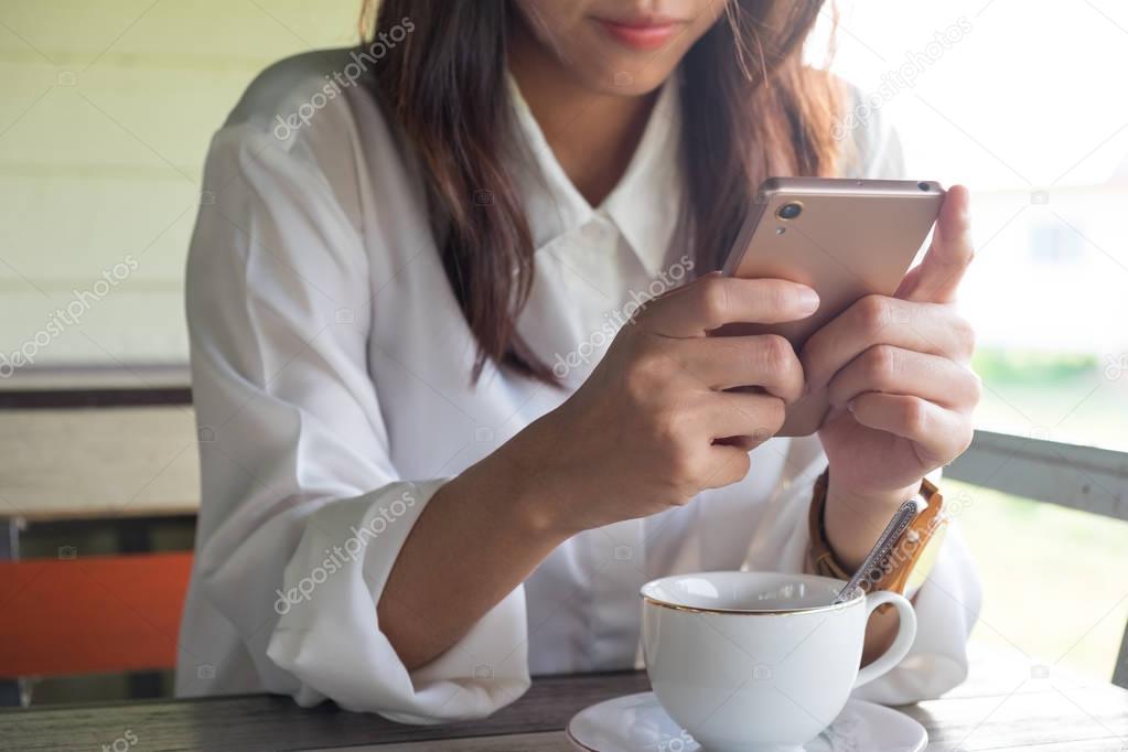 front view. young woman playing mobile phone while take a break in morning. front of her having coffee cup putting on wooden table. this image for business, technology, beverage and portrait concept