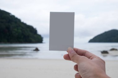 el ile sahilde beyaz Polaroid film ayakta tutan kadın
