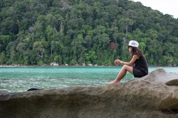 Mujer sentada en la roca. frente a ella tienen mar azul y verde —  Fotos de Stock