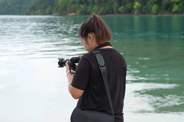 Mujer asia vistiendo camisa negra de pie en la playa y utilizando camer —  Fotos de Stock