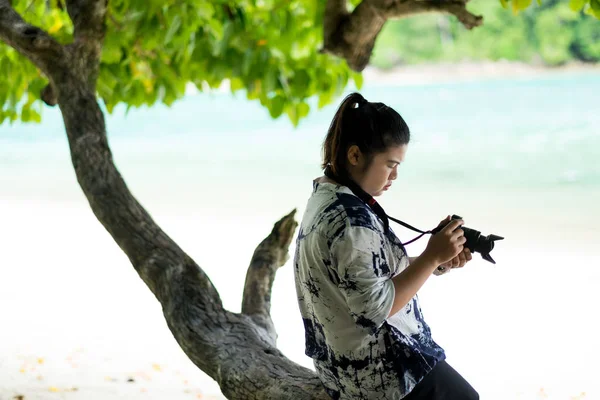 Asia mujer sentado en madera bajo el árbol y el uso de la cámara para tak —  Fotos de Stock