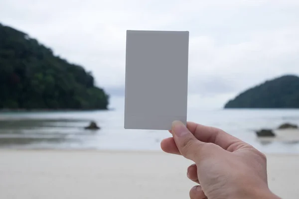 hand of woman holding white Polaroid film standing on beach with