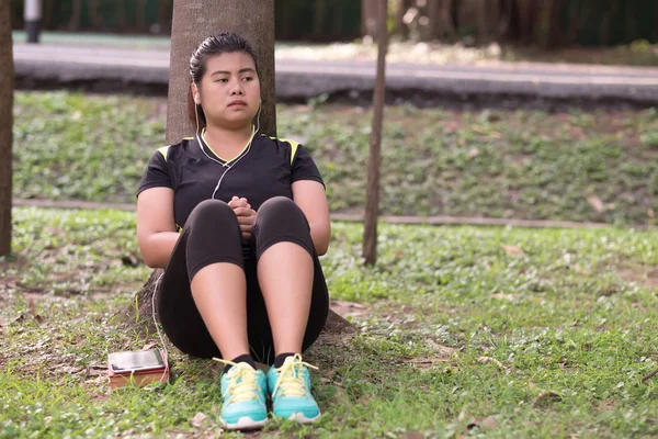 Mujer joven con auricular usando el teléfono para escuchar música y sentarse —  Fotos de Stock