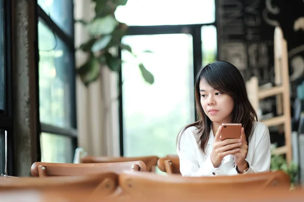 Jonge vrouwen zitten op houten tafel in de ochtend en het gebruik van mobiele — Stockfoto