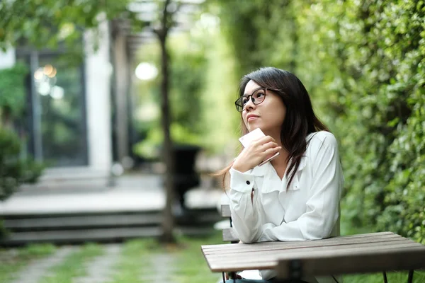 Mujer joven con gafas sentada en el jardín público verde. Ella... —  Fotos de Stock
