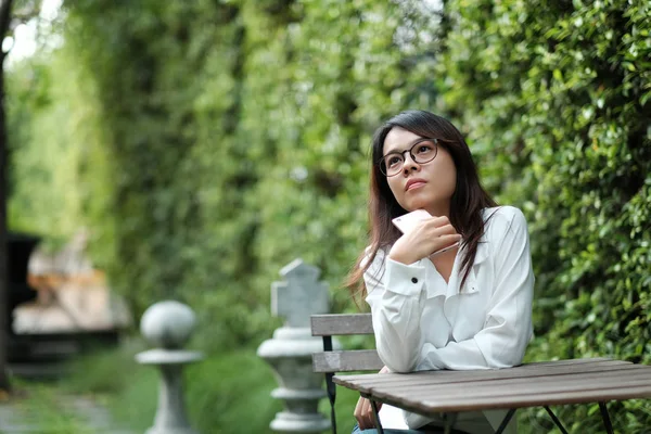 Mujer joven con gafas sentada en el jardín público verde. Ella... — Foto de Stock